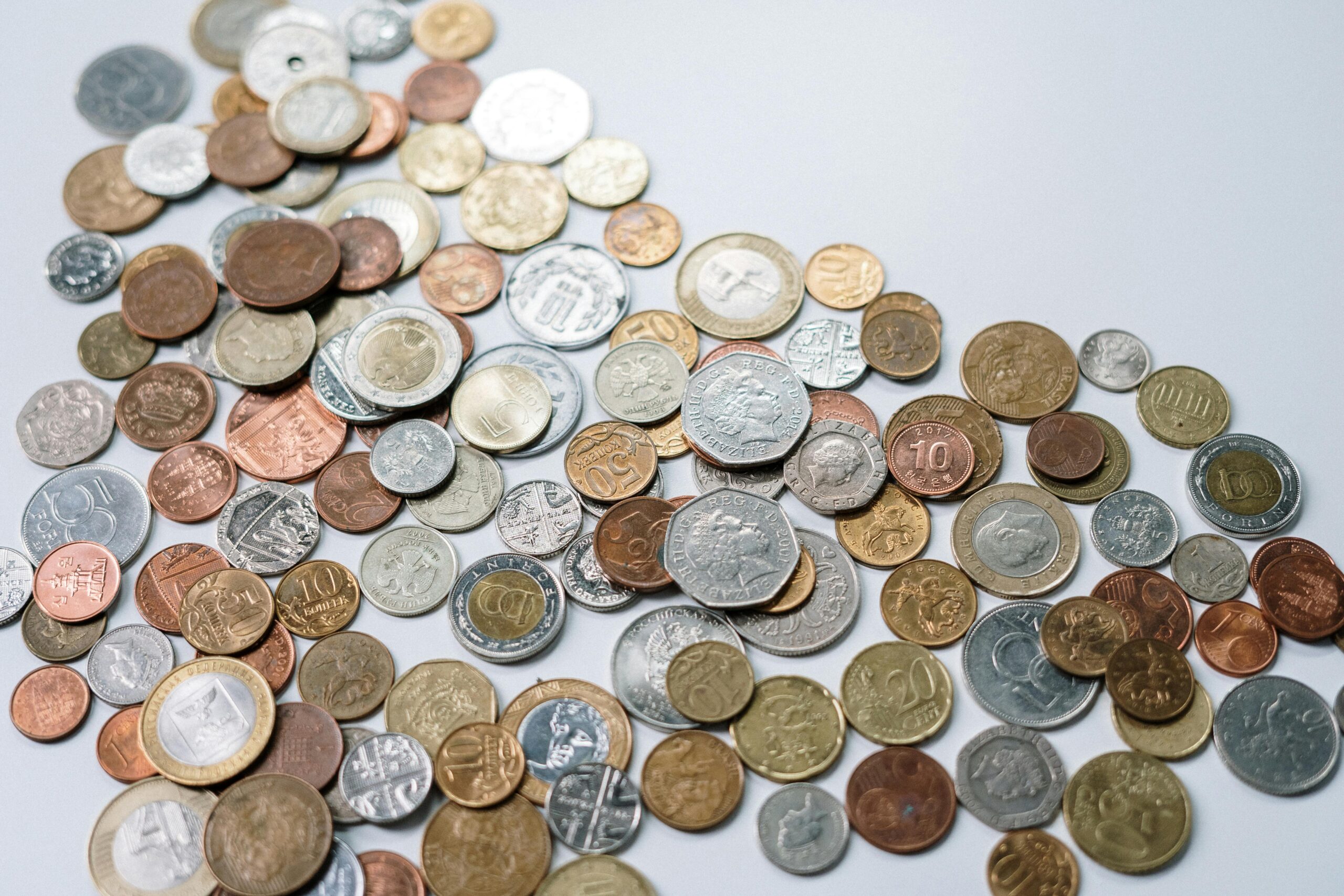 A variety of international coins scattered on a light background, showcasing different currencies.