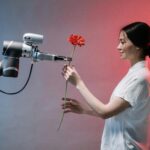 A woman interacts with a robotic arm holding a flower, symbolizing human-technology harmony.